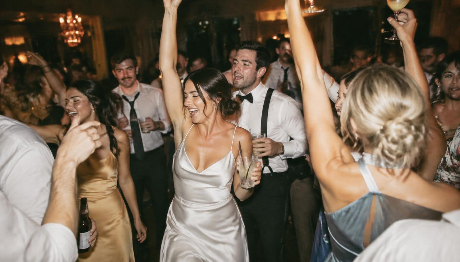 A packed wedding dance floor late at night with arms in the air